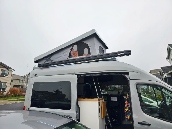 Gray rv rental with open pop-top tent (people inside), exterior awning, and compact interior kitchenette. Ideal for adventure.. Grit Overland GO A/T 2022