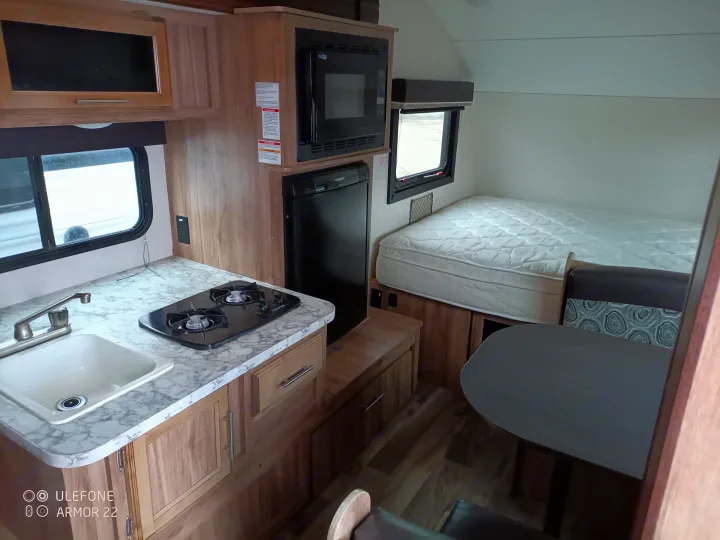 Inside an RV rental: a well-equipped compact kitchen, comfortable bed, and dining space, showcasing efficient design.. Jayco Hummingbird 2018