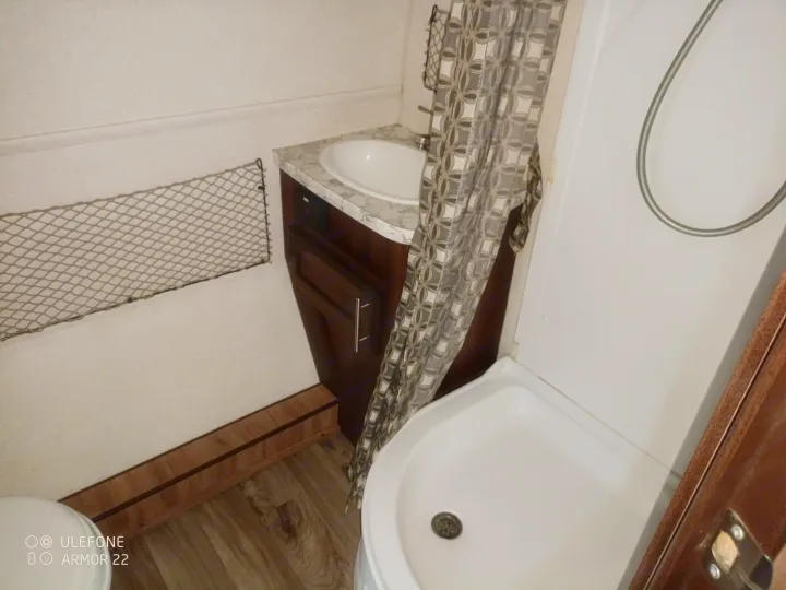 Compact RV rental bathroom interior, featuring a small sink, shower stall, and toilet, with a wall-mounted storage net.. Jayco Hummingbird 2018