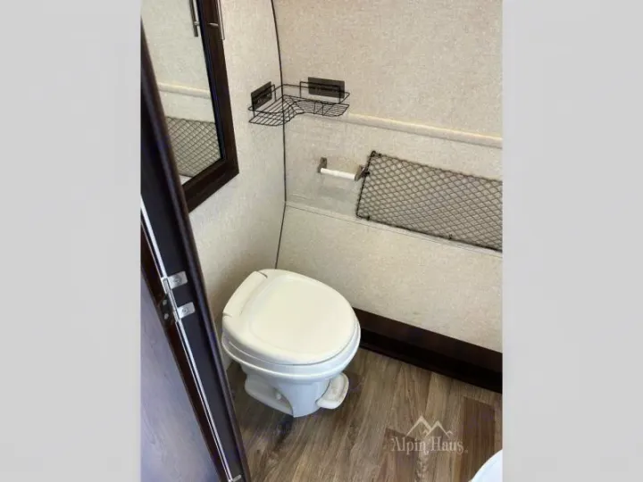 Inside an RV rental: a practical, compact bathroom with a white toilet, mirror, mesh storage, and wire basket for your road trips.. Jayco Hummingbird 2018