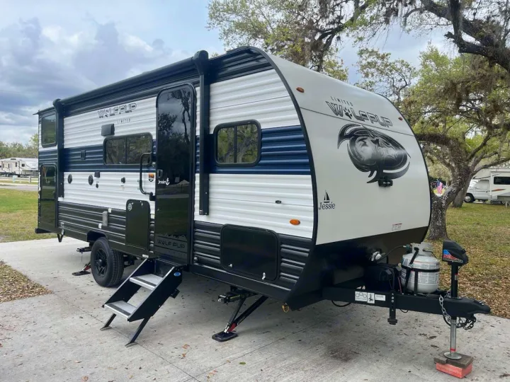 White & blue Wolf Pup travel trailer, Jessie, with steps down and stabilizers, ready for an RV rental at a campsite.. Forest River Wolf pup 17JW 2023
