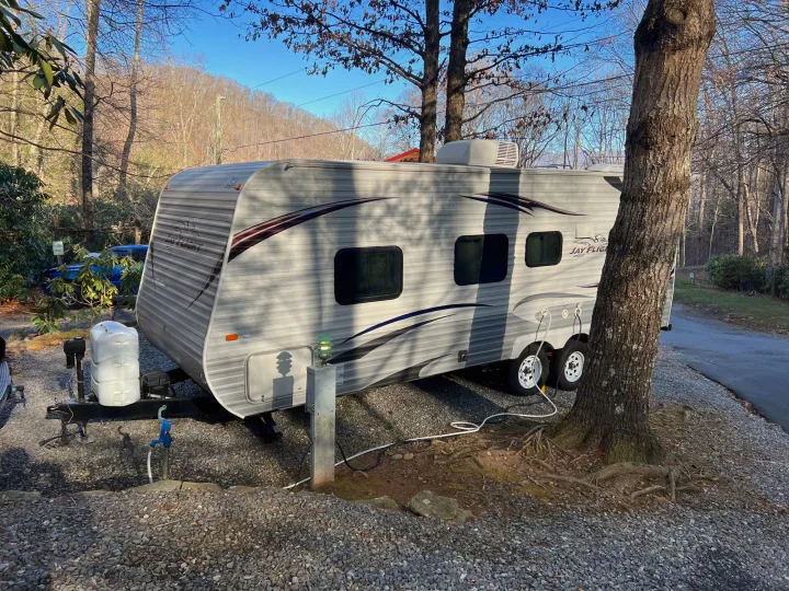 This grey travel trailer, ready with hookups at a gravel campsite, is ideal for an RV rental adventure.. Jayco Jay Flight 2013