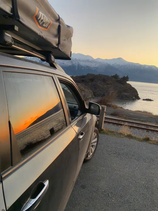 SUV with a Tepui rooftop tent by water and tracks, reflecting sunset over snow mountains. Perfect for your next RV rental adventure.. Subaru Forester X Premium 2011