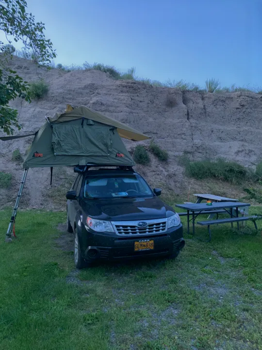 Black Subaru Forester with a Tepui rooftop tent set up for camping near cliffs, a versatile RV rental alternative for outdoor adventures.. Subaru Forester X Premium 2011