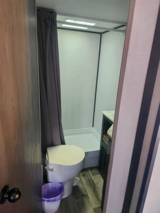 Compact RV rental bathroom features a white toilet, gray shower curtain, and small vanity for travel comfort.. Forest River ASPEN TRAIL 2024
