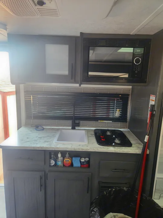 Functional RV rental kitchen: compact sink, stovetop, microwave, and gray cabinets with storage.. Forest River ASPEN TRAIL 2024