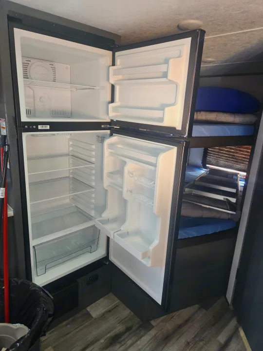 This RV rental features an empty, open two-door refrigerator with shelves and a crisper, next to built-in bunk beds.. Forest River ASPEN TRAIL 2024