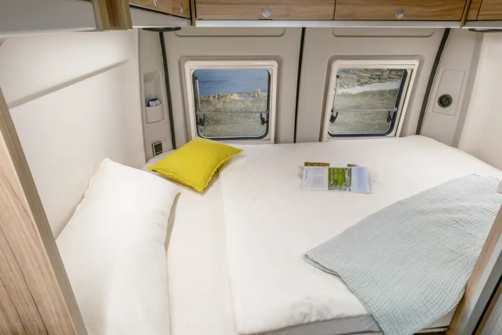 Comfortable RV rental bedroom with a cozy bed, pillows, and serene sea views from twin windows. Perfect for camper adventures.. Hymer Ayers Rock 2024