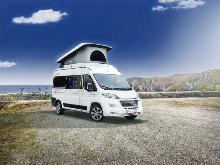 An rv rental white pop-top camper van, with bikes nearby, parked on a gravel coastal spot overlooking the sea and cliffs.. Hymer Ayers Rock 2024