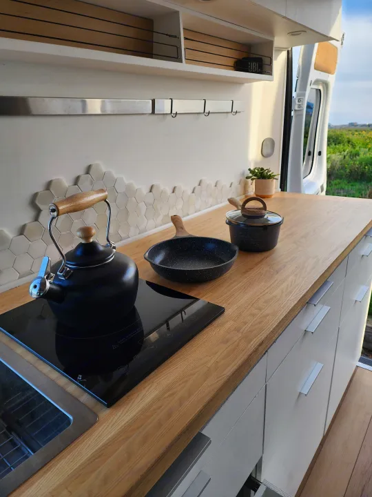 Compact and modern RV kitchen with wooden countertop, induction cooktop, kettle, and storage. Great for an RV rental getaway.. Dodge Sprinter Van 2015