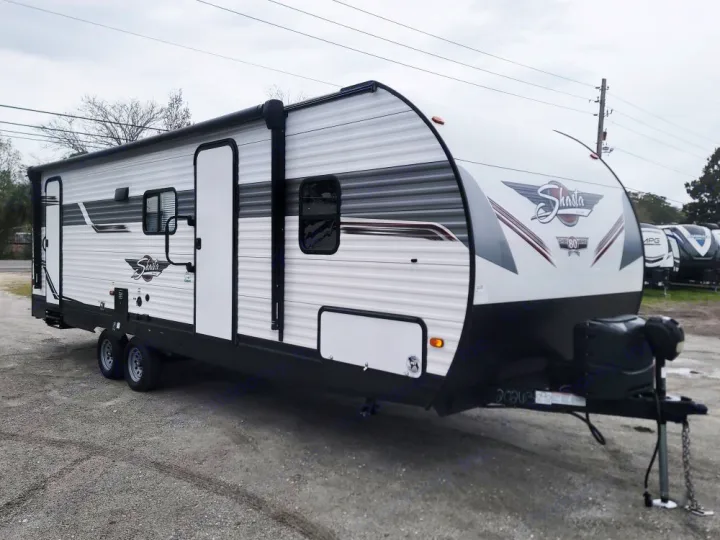 A new white Shasta travel trailer with gray and maroon stripes, parked on a gravel lot, available for RV rental.. Forest River Shasta 2022