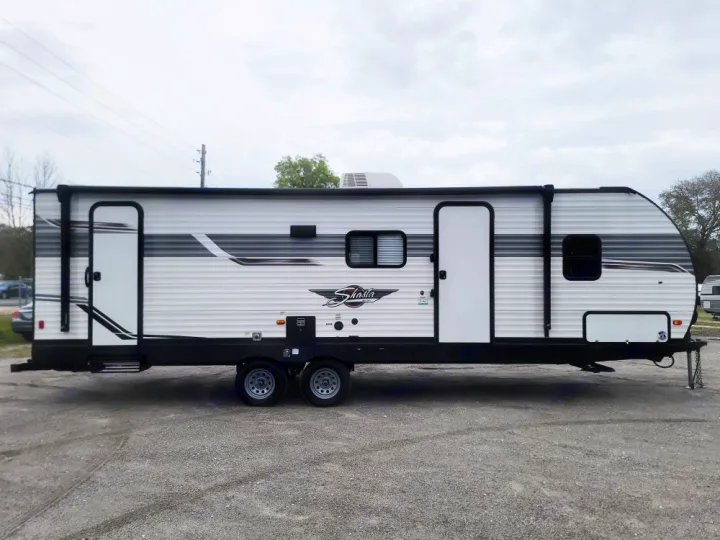 Side view of a white & gray Shasta travel trailer with two doors & awning, ideal for RV rental & camping adventures.. Forest River Shasta 2022