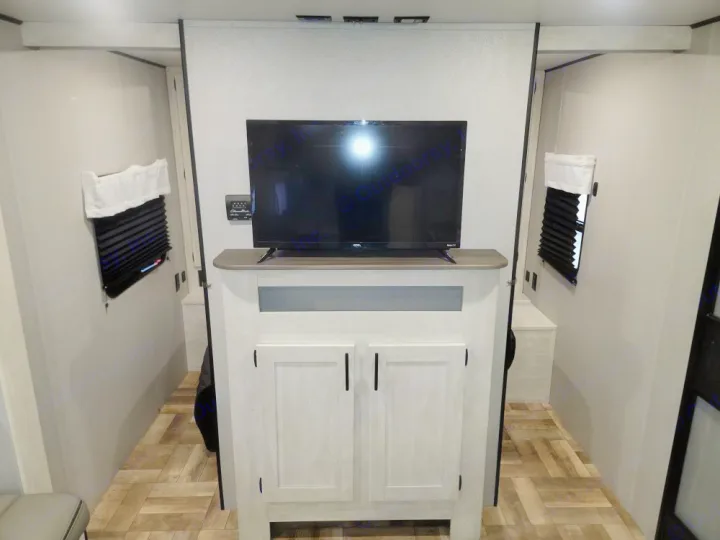 RV rental interior showing a central TV console atop light-colored cabinets, flanked by two narrow passages to sleeping areas.. Forest River Shasta 2022