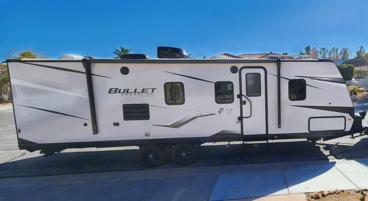 This white Bullet Crossfire travel trailer, perfect for an RV rental adventure, is ready for a road trip under a clear sky.. Keystone RV Bullet Crossfire 2022