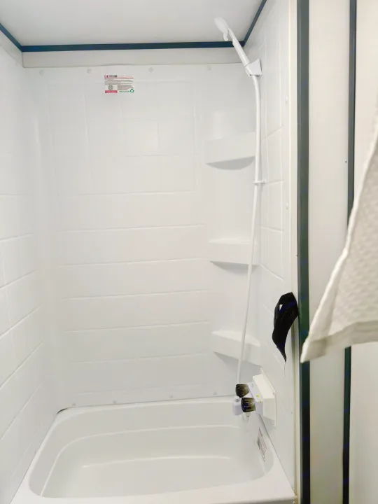 Compact white shower with a small tub and handheld shower head, perfect for an RV rental bathroom.. Keystone RV Bullet Crossfire 2022
