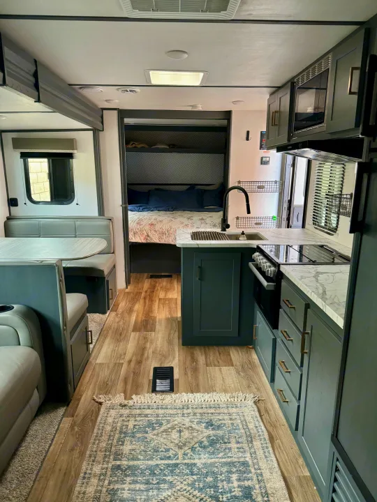 Modern RV rental interior with a gray kitchen, dining booth, and cozy bunk beds. Features wood-look flooring and a patterned rug.. Keystone RV Bullet Crossfire 2022