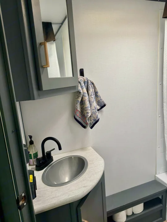 RV rental bathroom: Modern grey and white interior with sink, black faucet, mirror, towel, and toilet paper storage.. Keystone RV Bullet Crossfire 2022