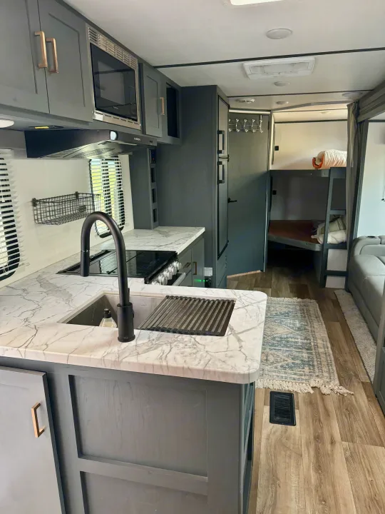 Inside a spacious RV rental: modern kitchen with gray cabinets, marble counters, and black fixtures, plus bunk beds visible in the back.. Keystone RV Bullet Crossfire 2022