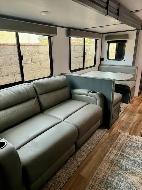 Modern RV rental interior with a grey sofa, dinette, and large windows, offering a comfortable and functional travel space.. Keystone RV Bullet Crossfire 2022