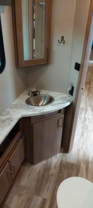 This RV rental bathroom features a stainless steel sink, marble-look counter, wood vanity, and mirrored cabinet.. Grand Design Imagine 2021