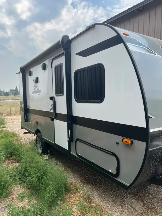 This white and gray Jay Flight SLX travel trailer, perfect for an RV rental, is parked outdoors, showcasing its side with an awning, door, and windows.. Jayco Jay Flight SLX 2023