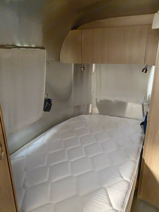 RV rental: Compact bedroom with a plush white mattress and modern wooden cabinetry inside a shiny metal-walled camper.. Airstream Flying Cloud 2018