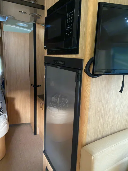RV rental interior: modern kitchen features a microwave, Dometic fridge, and TV. Light wood cabinets and cozy living space.. Airstream Flying Cloud 2018