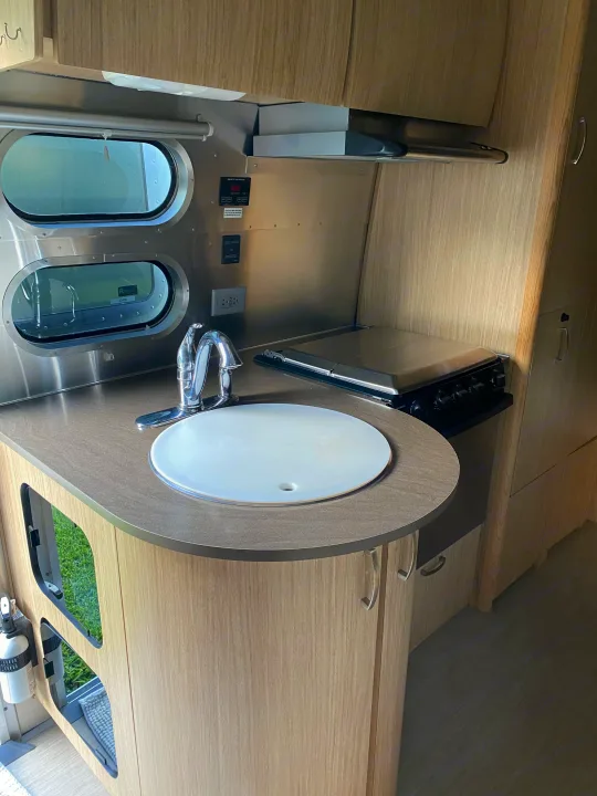 Modern rv rental kitchenette: Features a sink, covered stove, light wood cabinetry, and distinctive oval windows.. Airstream Flying Cloud 2018