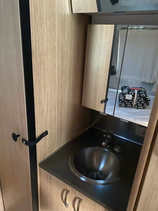 Compact RV rental vanity with a small sink and mirror. The mirror reflects a bed, highlighting its space-saving design.. Airstream Flying Cloud 2018