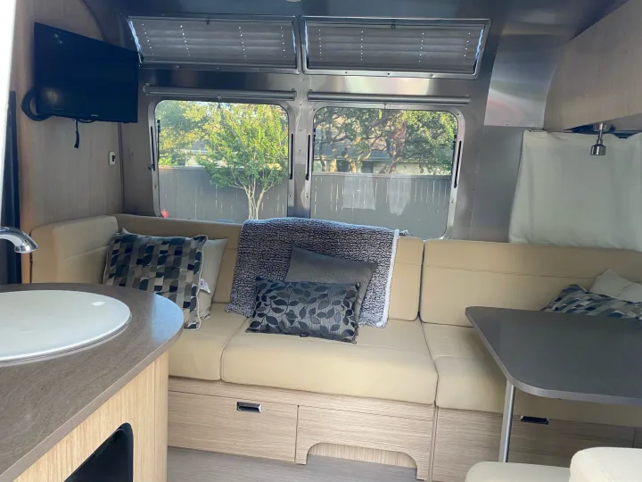 Explore this RV rental's inviting interior: tan seating, dining table, wall-mounted TV, and scenic windows.. Airstream Flying Cloud 2018