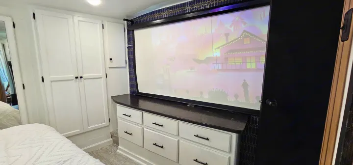RV rental bedroom featuring white cabinets, a dresser, and a large projector screen displaying a colorful image.. Heartland Edge 2016