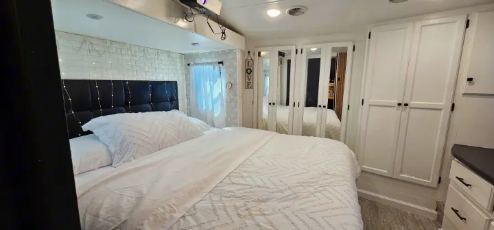 Spacious RV rental bedroom with white bedding, black headboard, and projector. Mirrored closet doors reflect the bed.. Heartland Edge 2016
