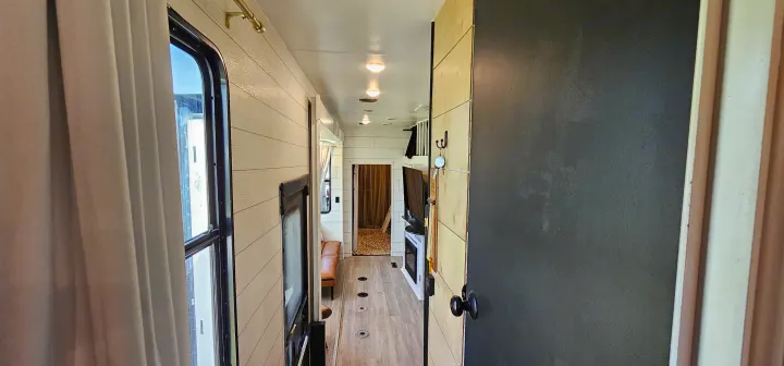 RV rental interior hallway: light wood-paneled walls, windows with curtains, and a view towards the living area.. Heartland Edge 2016