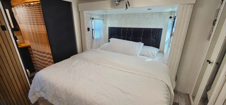 Cozy RV rental bedroom with white bedding, a black headboard, and decorative string lights, perfect for travel.. Heartland Edge 2016
