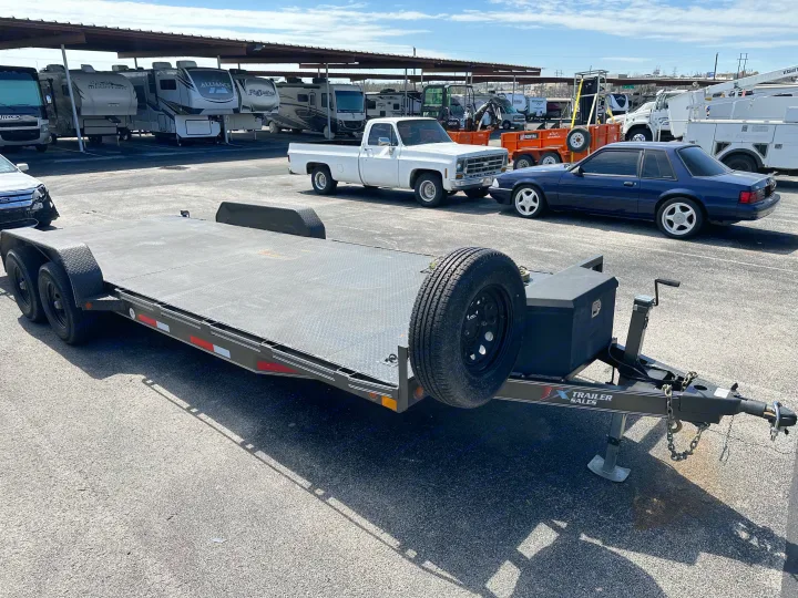 Large flatbed trailer shown with various RVs and vehicles in a sales/rv rental lot, mostly shaded from above.. East Texas Trailers Car Hauler 2021