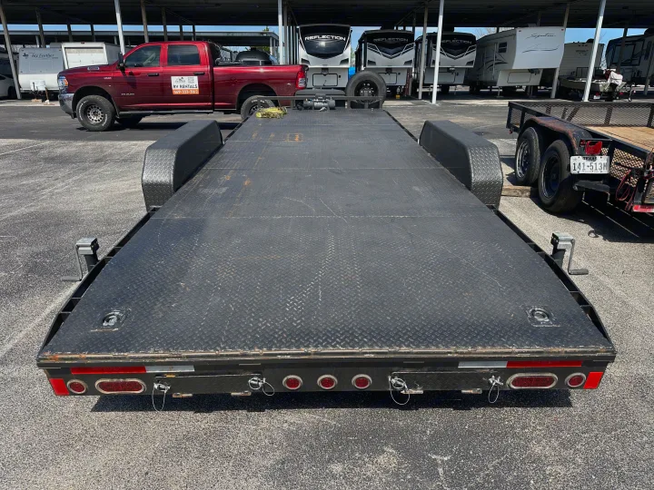 Flatbed trailer in front of a red RV rental truck and several RVs/travel trailers under a covered lot.. East Texas Trailers Car Hauler 2021