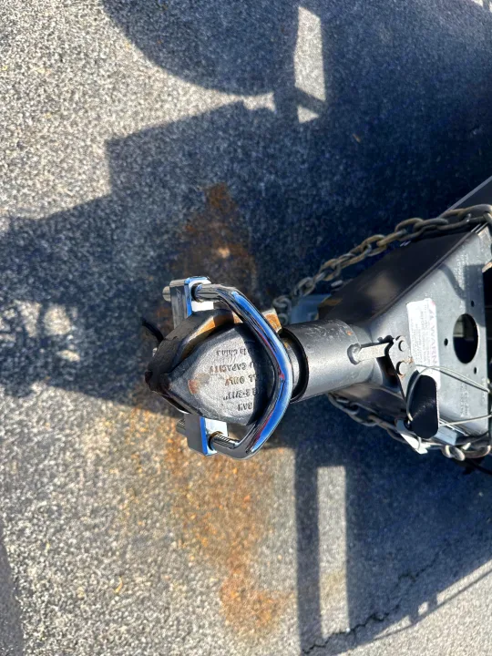Trailer hitch secured for RV rental towing with coupler lock and safety chains. Pavement with shadows and rust.. East Texas Trailers Car Hauler 2021