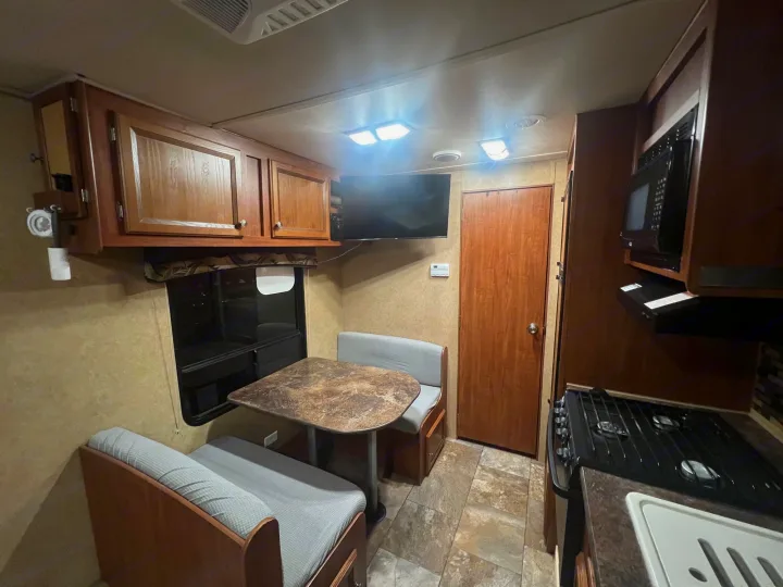 Comfortable rv rental interior featuring a dinette, kitchen with microwave, stove, TV, and overhead cabinets.. Jayco Jay Flight 2013