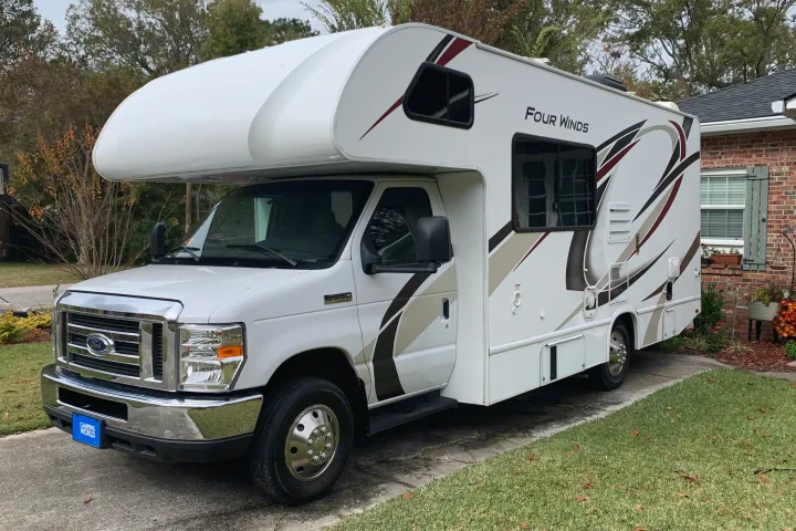 This large white Class C RV rental, a Thor Four Winds, is parked on a driveway, ready for camping adventures.. Thor Four Winds 2020