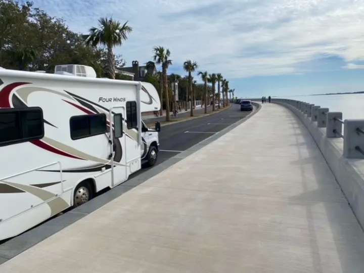 A Four Winds RV rental is parked along a sunny, palm-lined waterfront promenade overlooking a wide bay.. Thor Four Winds 2020