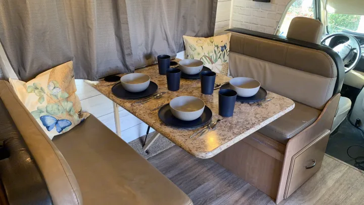 Inside an RV rental: a modern dinette with light-colored booth seating, a speckled table set for four, and front cabin visible.. Thor Four Winds 2020