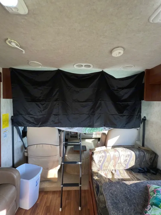 View inside an RV rental, showing the front cab with a black privacy curtain, ladder, and living area.. Storm Storm Motorhome 2011