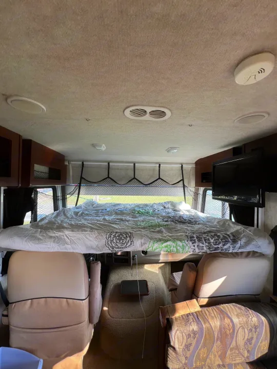 RV rental interior featuring a cab-over bunk bed with safety net, front seats below, and a mounted TV.. Storm Storm Motorhome 2011