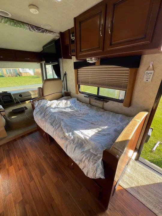 Experience comfortable travel in this rv rental. View of a cozy bed, driver's cockpit, and warm wood flooring inside an RV.. Storm Storm Motorhome 2011
