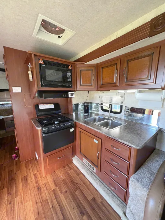 RV rental kitchen with microwave, stove, double sink, and wood cabinets. Perfect for mobile living & cooking on the road.. Storm Storm Motorhome 2011