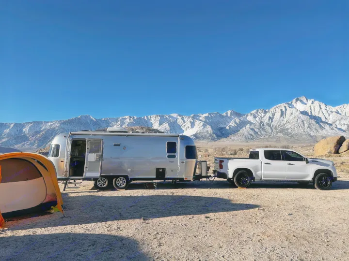A silver Airstream travel trailer and white pickup truck, with an orange tent, are parked against snowy mountains. Perfect for your RV rental adventure.. Airstream Flying Cloud 2017