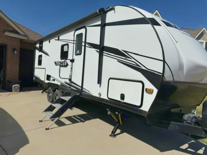 A white and black travel trailer with steps extended and jacks down is parked on a driveway, ready for an rv rental trip.. Forest River Tracer 2022