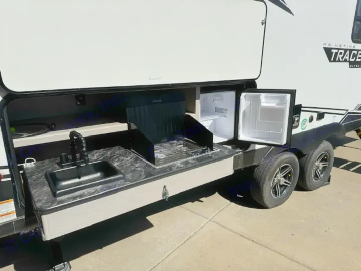 An RV rental's outdoor kitchen, extended from the side, features a sink, grill, and two open mini-fridges.. Forest River Tracer 2022