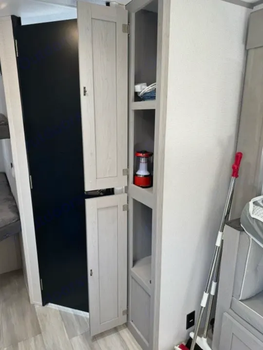 RV rental interior: A light wood storage cabinet with open shelves holding items like a red lantern. Black door and seating visible.. Forest River Tracer 2022