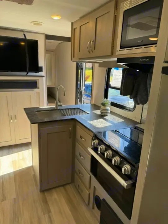 Modern RV rental interior with a well-equipped kitchen (microwave, stove, sink) and adjacent living area with TV.. Forest River Tracer 2022